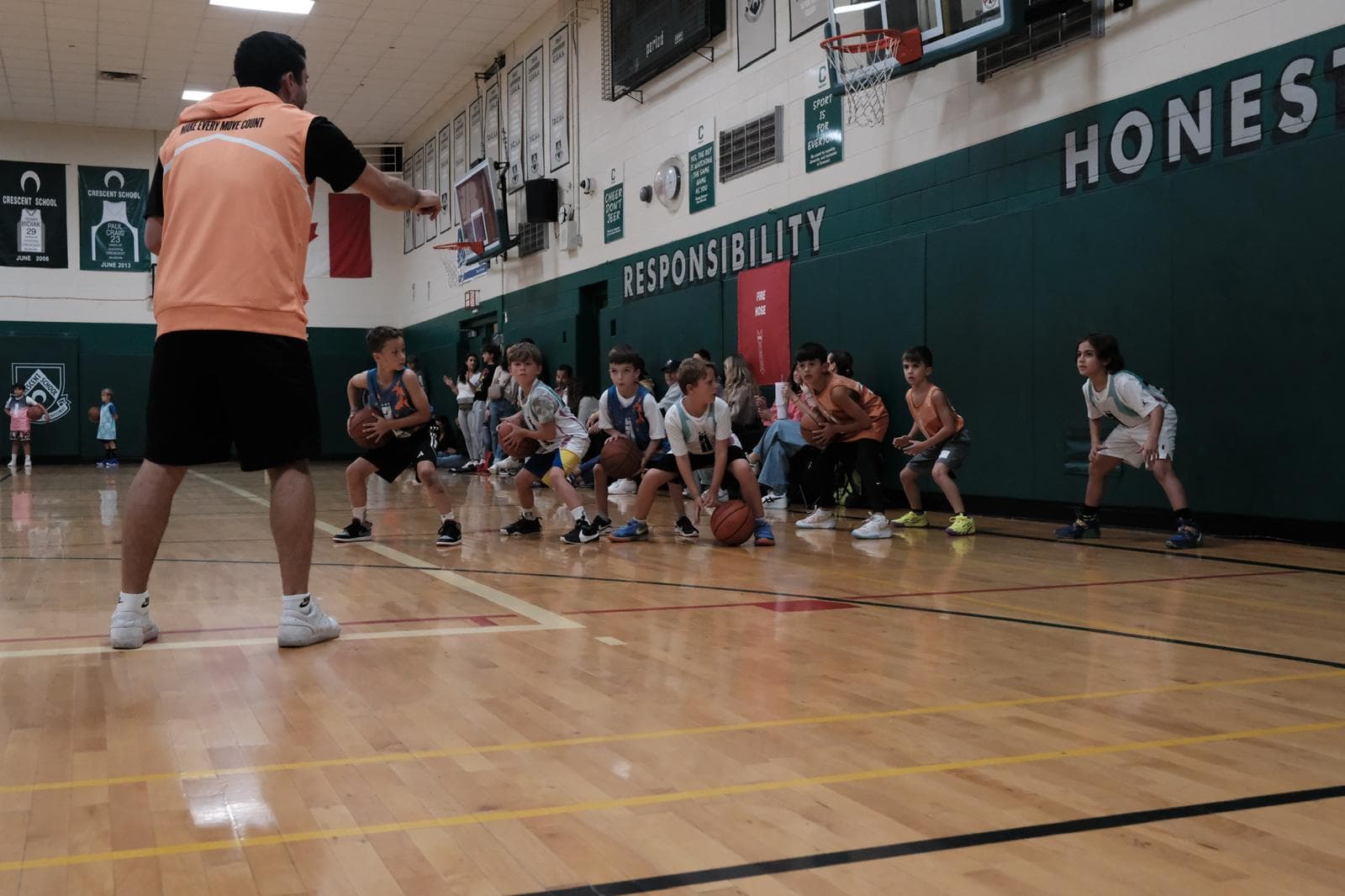 A 3BA coach in an orange pinnie leading a line of young students through a ball-handling drill