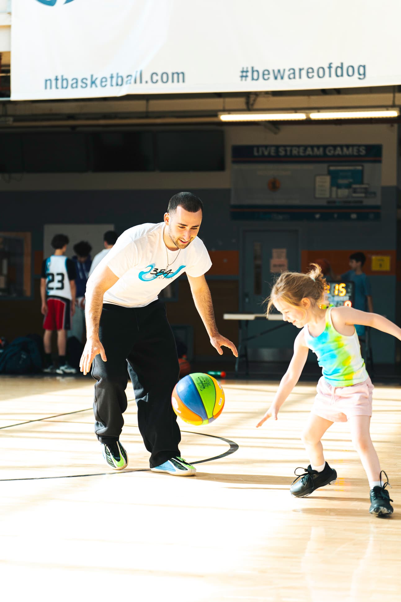 A 3BA coach playing light defense while a small child dribbles past him, both laughing