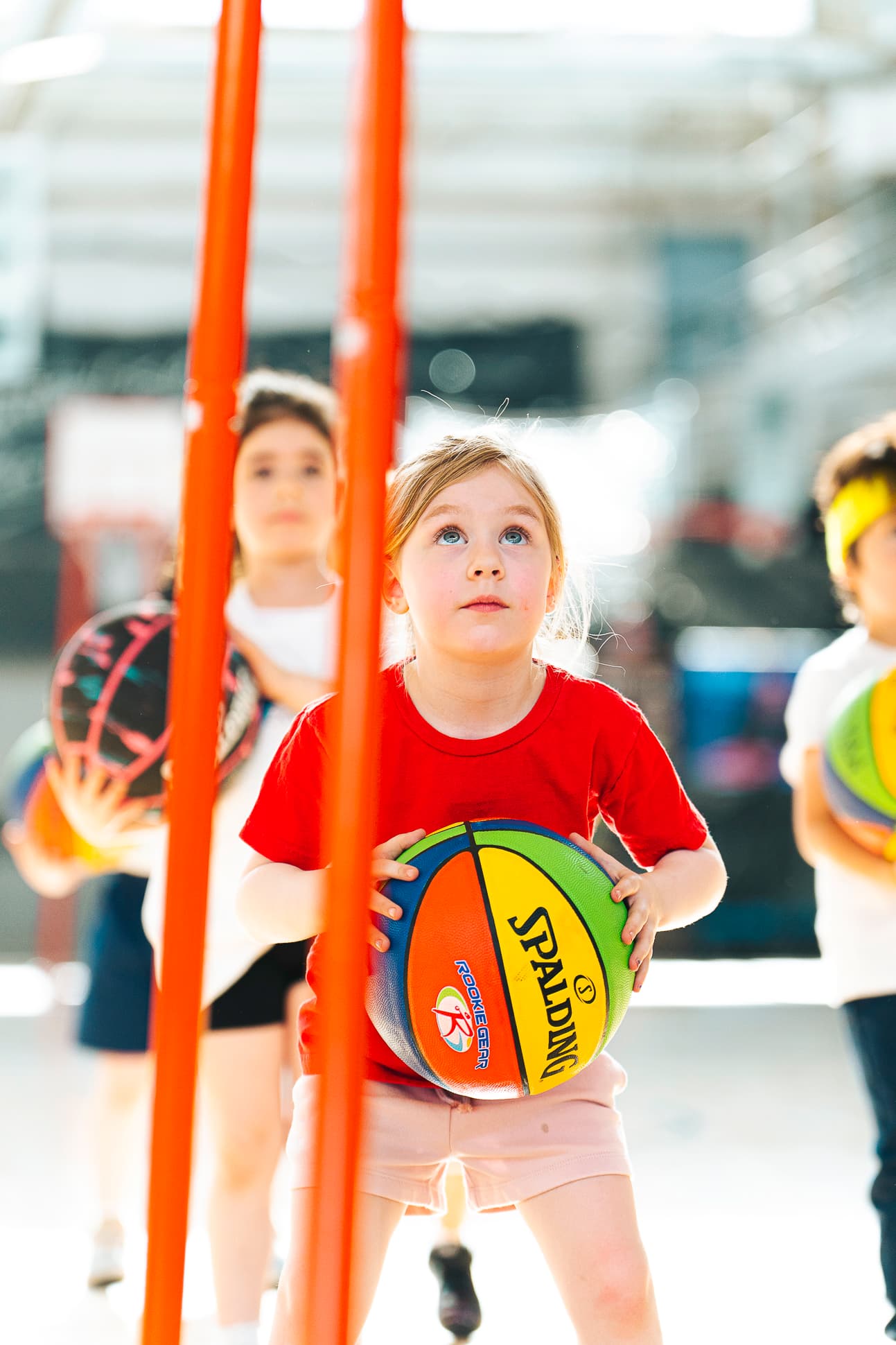A young athlete holding a rainbow basketball at her chest with her eyes fixed on the rim