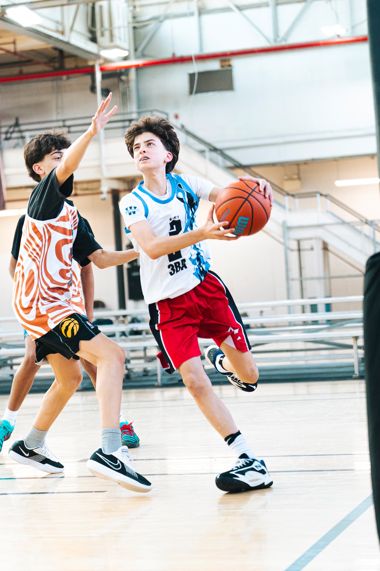 A Youth division player in a white 3BA jersey attacking the rim past a defender